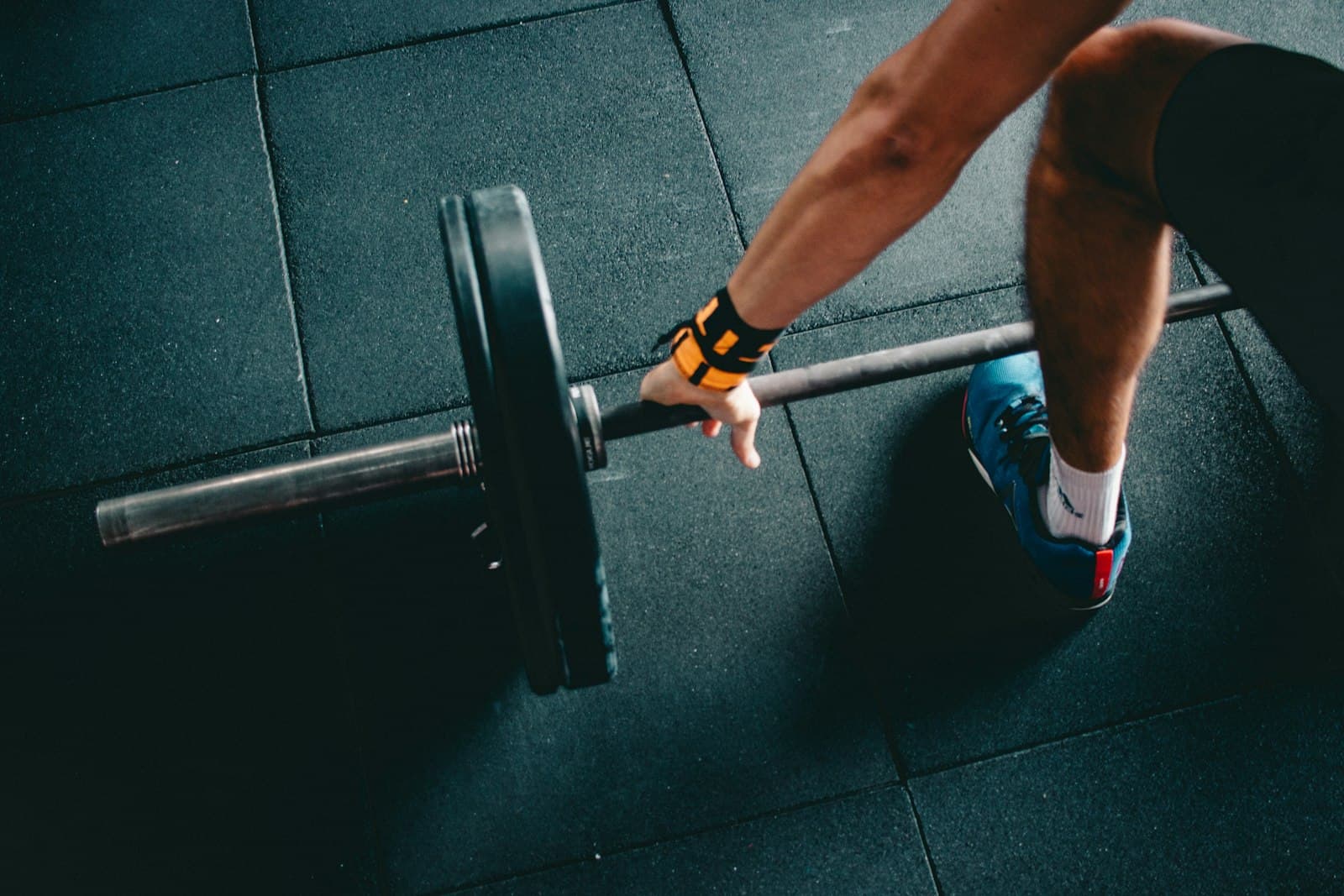 Loaded barbell mid-pull from overhead view with orange wrist wrap