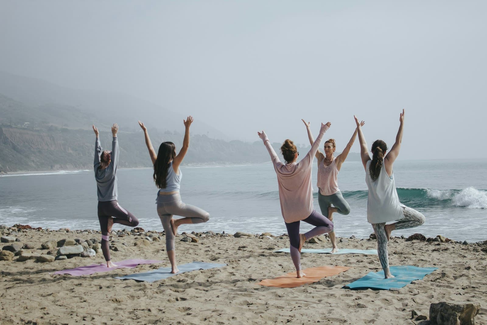 Group yoga tree pose on a sunlit beach